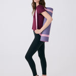Lolë Pose yoga mat in lavender purple, a woman carries the rolled mat at her side by its pink strap