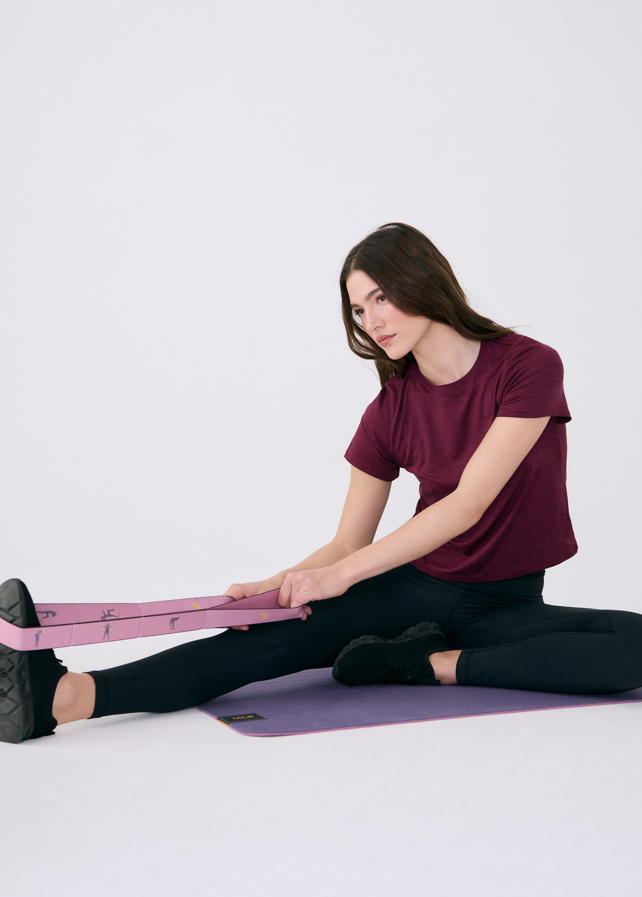 Lolë Pose yoga mat in mauve purple, a seated woman stretches with the pink strap looped around her foot