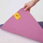 Lolë Pose yoga mat in orchid pink, a hand lifts one corner to reveal the navy underside beneath the pink top