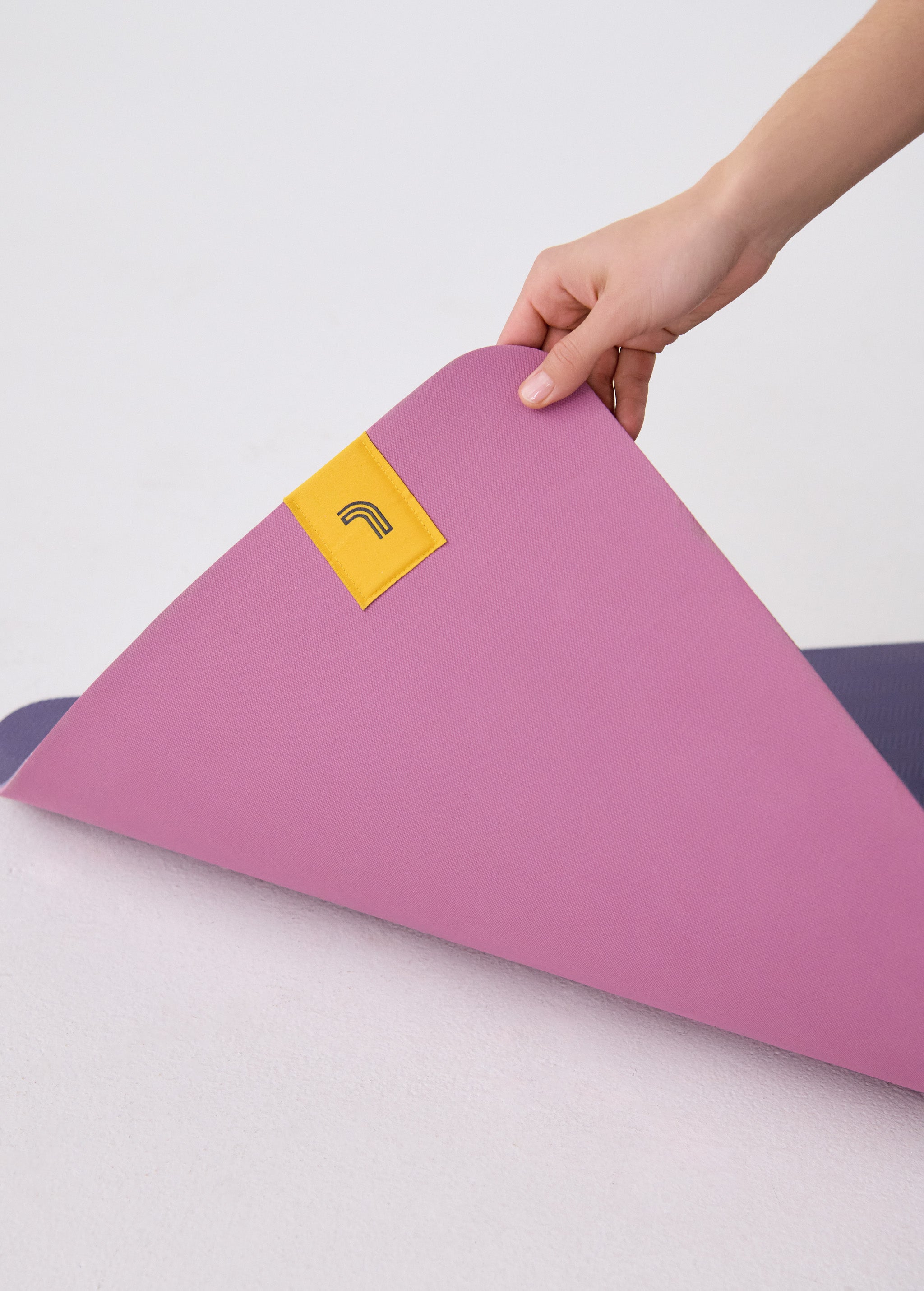 Lolë Pose yoga mat in orchid pink, a hand lifts one corner to reveal the navy underside beneath the pink top