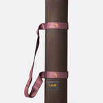 Lolë Pose yoga mat in chocolate brown, rolled and secured with the mauve carry strap