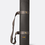 Lolë Pose yoga mat in charcoal, rolled up with the taupe shoulder strap looped for carrying