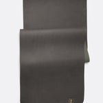 Lolë Pose yoga mat in charcoal, laid flat with charcoal surface up and olive green underside peeking underneath