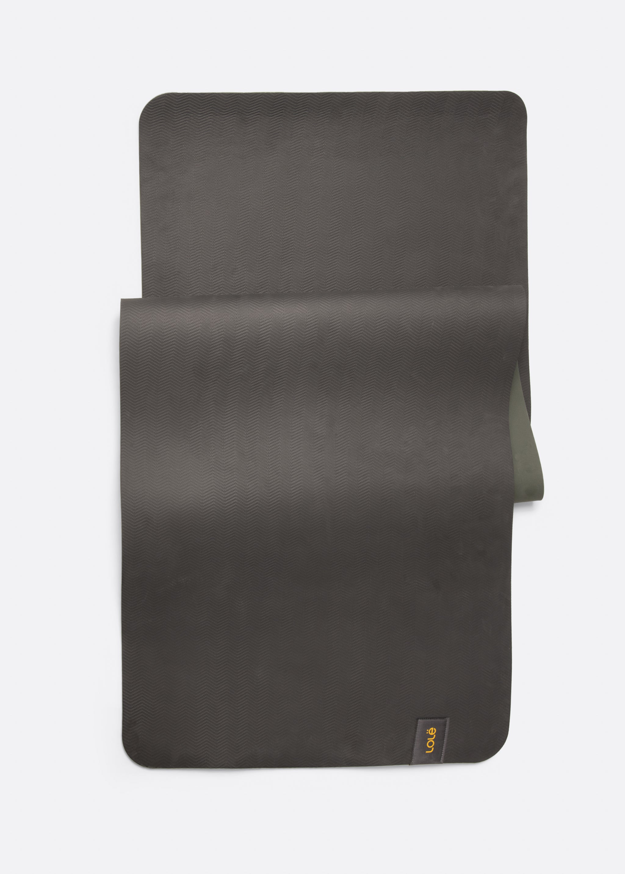Lolë Pose yoga mat in charcoal, laid flat with charcoal surface up and olive green underside peeking underneath
