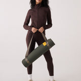 Lolë Pose yoga mat in olive green, carried over a woman's shoulder using the taupe strap