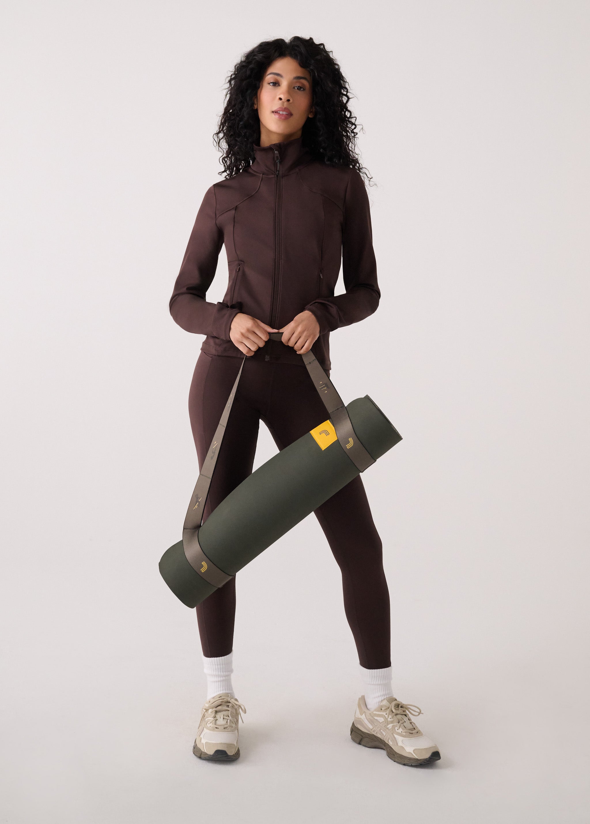 Lolë Pose yoga mat in olive green, carried over a woman's shoulder using the taupe strap