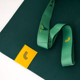 Lolë Pose yoga mat in forest green, close-up of a corner with the green strap coiled and yellow logo tag