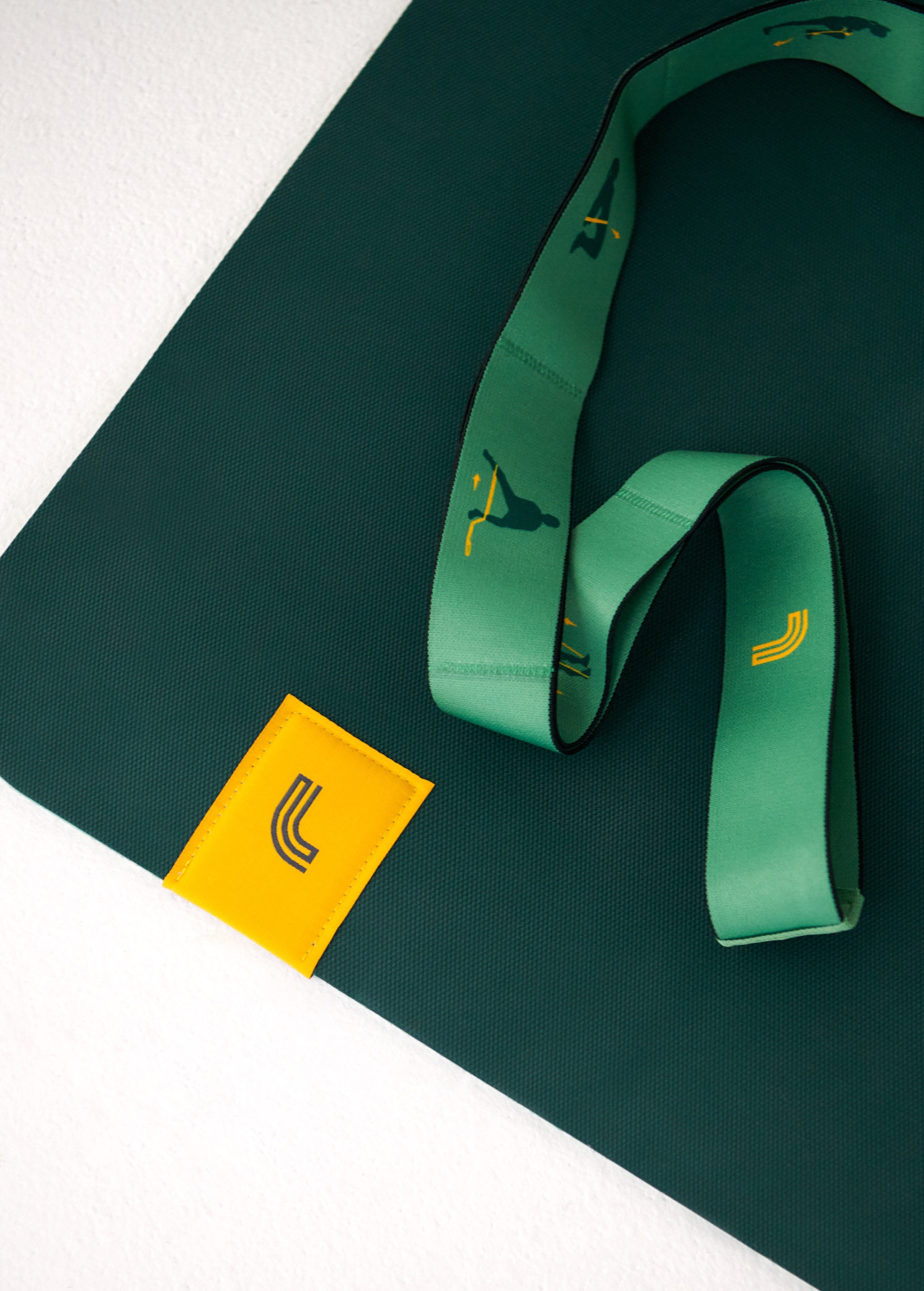 Lolë Pose yoga mat in forest green, close-up of a corner with the green strap coiled and yellow logo tag