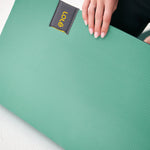 Lolë Pose yoga mat in sage green, close-up of a hand pressing the textured surface near the label