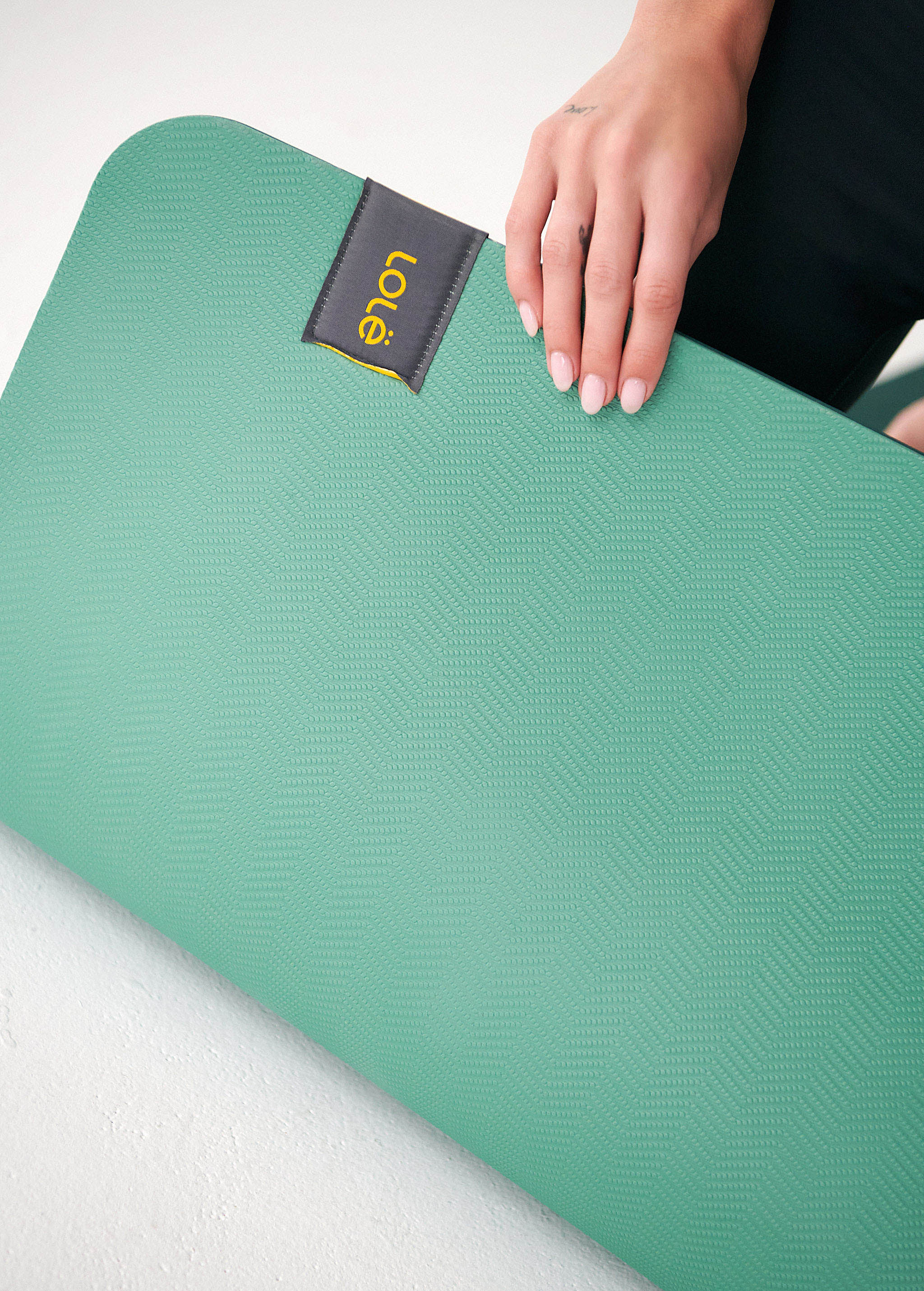 Lolë Pose yoga mat in sage green, close-up of a hand pressing the textured surface near the label
