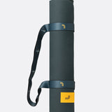 Lolë Pose yoga mat in dark teal, rolled up with the teal shoulder strap wrapped around it
