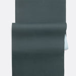 Lolë Pose yoga mat in dark teal, unrolled flat with teal top and pale ice-blue underside showing at the roll