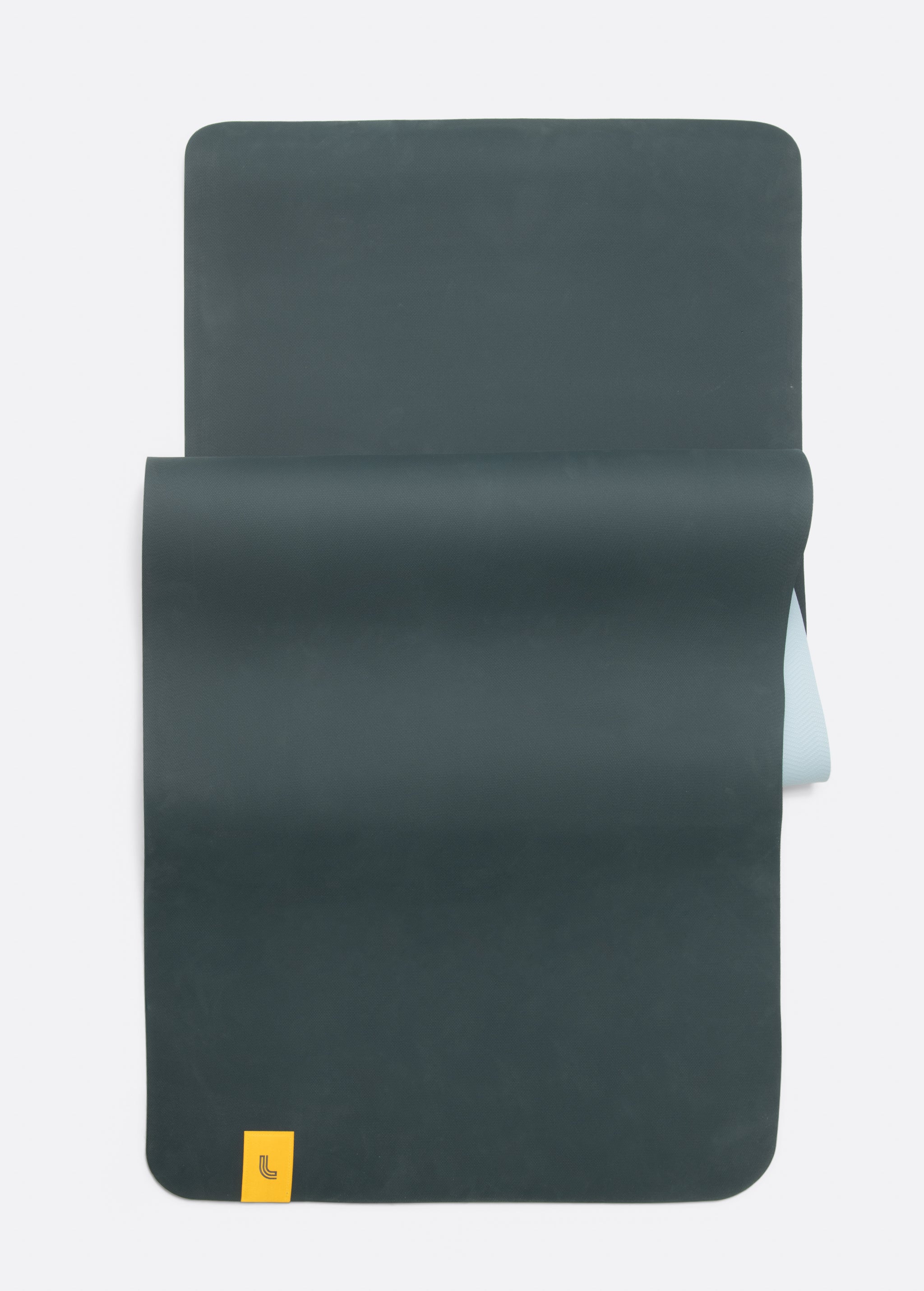 Lolë Pose yoga mat in dark teal, unrolled flat with teal top and pale ice-blue underside showing at the roll