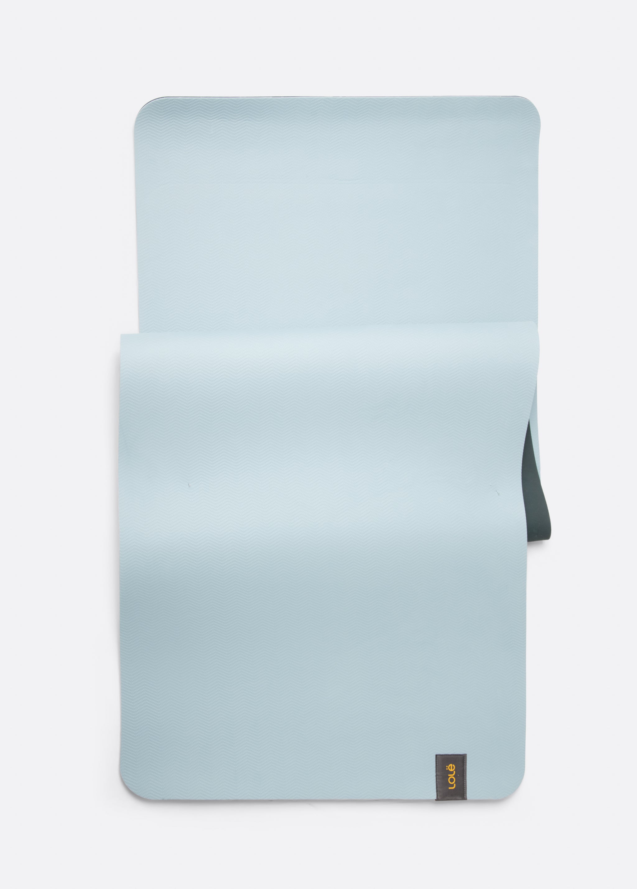 Lolë Pose yoga mat in pale ice blue, laid flat with ice-blue surface up and dark teal underside at the edge